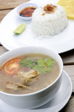 Pirzola çorbası bir kase içinde beyaz pirinç ve kırmızı biber sosuyla servis edilir.