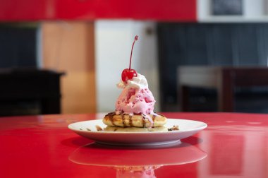 Kırmızı masaya konmuş kirazla süslenmiş dondurma krepleri.