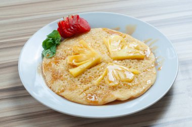 Beyaz tabakta servis edilen ve çilekle süslenmiş ananaslı krep.