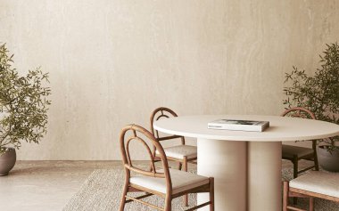 Tahta sandalyeler ve yeşilliklerle çevrili yuvarlak bir masanın üzerinde beyaz heykeltraş lambasıyla vurgulanmış minimalist bir yemek alanı.