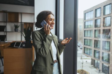 Yüksek bir binanın camının önünde resmi kıyafetler giymiş, bir etkinlik sırasında cep telefonuyla konuşan beyaz bir işçi duruyor.