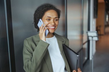 Resmi kıyafetli bir beyaz işçi, elinde dizüstü bilgisayarla kapıya yakın bir cep telefonuyla konuşurken gülümsüyor ve jest yapıyor. Etkinlik eğlenceli görünüyor ve yüzü kıllı.