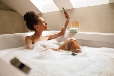 Bir kadın jakuzide selfie çekiyor, göğsünü ve kalçalarını saran sıcak suyun keyfini çıkarıyor.