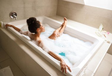 Bir kadın köpükle dolu bir küvette banyo yapıyor. Banyosundaki kompozit malzemelerden yapılmış tesisat tesisatının rahatlatıcı deneyimini yaşıyor.