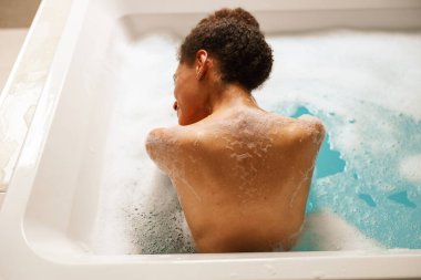 Bir kadın sıcak suyla dolu bir küvette banyo yapıyor. Köpük banyosunun keyfini çıkarıyor.