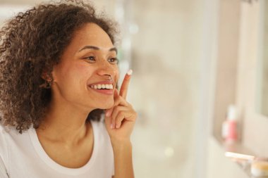 Kadın mutlu bir şekilde aynadaki yansımasına hayran. Gülüşünü, kaşlarını, kıvırcık saçlarını, çene çizgisini ve kirpiklerini fark ediyor. Kulaklarıyla dalga geçerken.