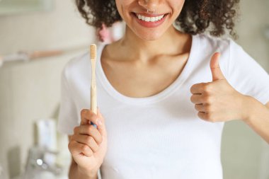 Bir kadın elinde diş fırçasını tutuyor ve iyi bir ağız hijyenini desteklemek için baş parmak işareti yapıyor. Ağzınıza, kaslarınıza, çenenize ve dişlerinize dikkat edin. Sağlıklı bir gülümseme ve genel olarak sağlıklı bir yaşam için.