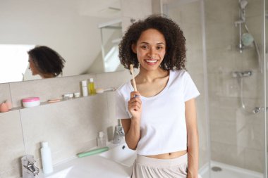 Kadın lavabonun önünde duruyor, bir gülümsemeyle dişlerini fırçalıyor. Banyo iç tasarımı, bina içinde bir pencere, tıkırtı ve kol hareketi içerir.