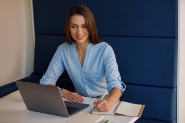 İş kadını modern ofise odaklanmış, dizüstü bilgisayarda yazıyor, not alıyor, üretkenlik ve profesyonelliği gösteriyor