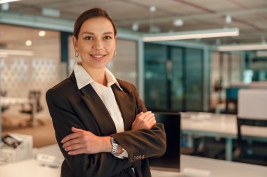 Kendine güvenen bir iş kadınının portresi modern bir ofis çalışma alanında duruyor, liderlik ve başarı yayıyor..