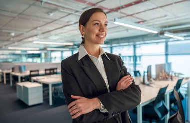 Kendine güvenen bir iş kadını modern bir açık alan ofis ortamında gülümsüyor, profesyonellik ve başarı yayıyor.