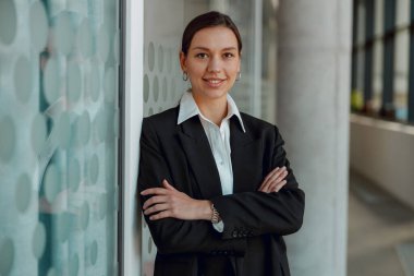 Kendine güveni tam bir iş kadını modern ofiste kollarını kavuşturarak poz veriyor, profesyonel bir portre.