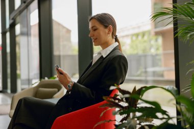 A businesswoman uses smartphone in a modern office lounge, showing a successful and techsavvy career environment clipart