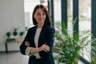 Modern ofisteki kendine güvenen iş kadını, şık giyinen, çapraz kollarla duran, azimli.