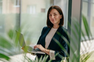 Kendine güvenen bir iş kadını, modern bir ofiste verimli bir iş hayatı dengesi olan bir dizüstü bilgisayar kullanır..