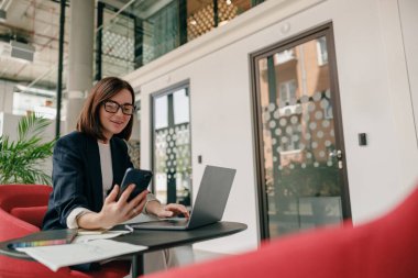 Şık bir ofiste dizüstü bilgisayarı ve akıllı telefonu olan profesyonel bir kadın verimliliği ve verimliliği somutlaştırır.