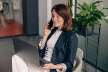 Kendine güvenen bir iş kadını, modern ofis ortamında dizüstü bilgisayar üzerinde çalışırken birden fazla iş yapıyor.