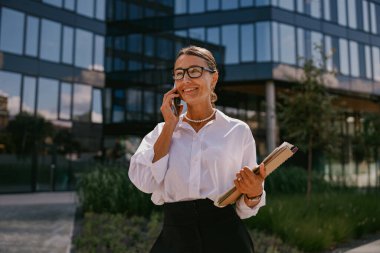 İş ortamında, kendine güvenen bir kadın önemli bir belgeyi tutarken önemli bir telefon görüşmesi yapar.