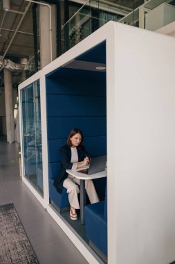 Modern ofis standında çalışan odaklanmış bir kadın üretkenlik ve konsantrasyon için sessiz bir alan kullanıyor..