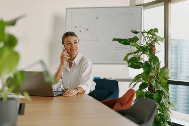 Modern ve şık bir ofiste otururken telefonla konuşan profesyonel bir kadın.