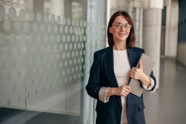 Gözlüklü kendine güvenen iş kadını modern ofiste bir tablet tutuyor, hırs ve profesyonelliği somutlaştırıyor.