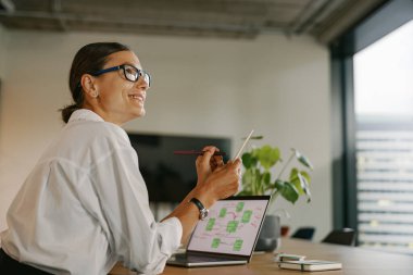 Profesyonel bir kadın gülümserken özenle dizüstü bilgisayarı üzerinde çalışıyor.
