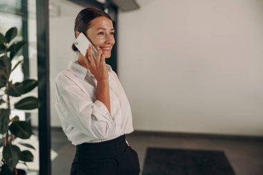 Sofistike bir ofis alanında telefonla konuşurken kendine güvenen bir iş kadını ışıl ışıl gülümsüyor.