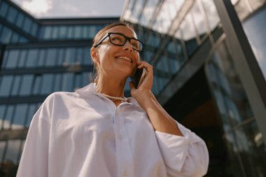 Modern cam ofis binasına yakın bir yerde telefonla konuşan profesyonel bir kadın.