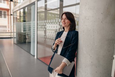 Modern bir ofiste dizüstü bilgisayarı ve kahvesiyle donanma ceketi giyen profesyonel bir iş kadını..