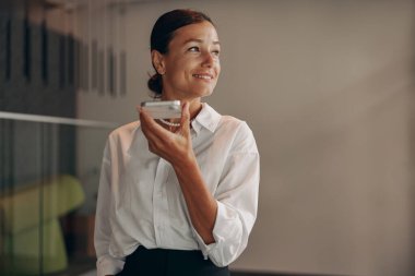 Günümüz ofis ortamında, profesyonel bir kadın gülümsüyor ve telefonda sohbet ediyor.