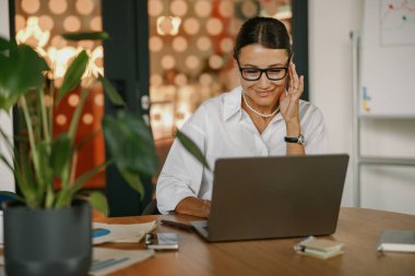 Kendini işine adamış, profesyonel bir kadın modern ve şık bir çalışma ortamında laptopuyla aktif olarak meşgul oluyor.