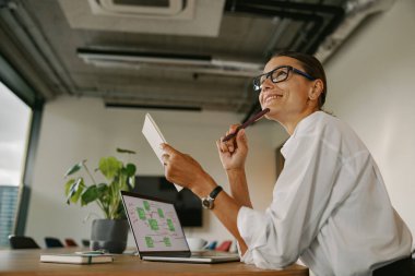 Modern bir ofis ortamında odaklanmış ve kendini işine adamış bir kadın. Dizüstü bilgisayarında yaratıcı işleriyle çok meşgul.