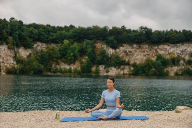 Etrafı canlı yemyeşil bir gölle çevrili sakin bir gölde huzur içinde meditasyon yapan bir kadın.