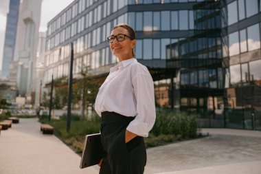 Kendine güvenen bir iş kadını modern bir şehir ortamında duruyor, kendi tarzında profesyonellik ve zarafet yayıyor.