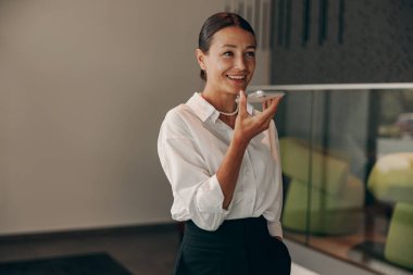 Şık giyinmiş bir kadın. Çağdaş bir ofis ortamında telefonla konuşurken ışıl ışıl gülümsüyor.
