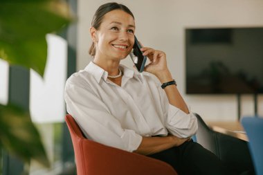 Kendine güvenen ve kendine güvenen bir kadın şık ve modern bir ofis ortamında telefonla konuşmaktan hoşlanır.