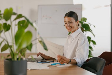 Kendini işine adamış ve işine odaklanmış bir profesyonel şık bir ofiste çeşitli önemli belgeleri özenle analiz ediyor.