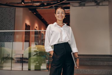 Modern bir ofis ortamında, dengeli ve iyi giyimli bir iş kadını uzmanca profesyonelliğini sergiliyor.