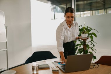 Genç bir profesyonel, üretkenlik için tasarlanmış parlak ve modern bir ofis ortamında özenle dizüstü bilgisayarına odaklanır.