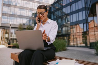 Uzaktan kumandalı bir işte çalışan profesyonel bir kadın, telefon görüşmelerini ve dizüstü bilgisayar görevlerini dengeliyor..