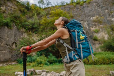 Bir kadın açık havada olmaktan zevk alıyor, büyük bir sırt çantasıyla yürüyüşe çıkıyor ve muhteşem bir manzarada yürüyüş direkleriyle yürüyor.