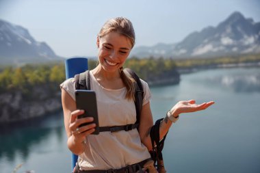 Neşeli ve gülümseyen bir yürüyüşçü muhteşem doğal bir manzarada akıllı telefonuyla güzel bir anı yakalar.