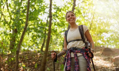 Neşeli bir kadın yemyeşil bir ormanda yürüyüş yapar, doğa harikalarını ve doğa macerasının heyecanını gösterir.