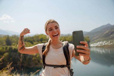 Genç bir kadın, doğa güzelliğinin ortasında güzel bir selfie çekerken yürüyüş başarısını sevinçle kutluyor.