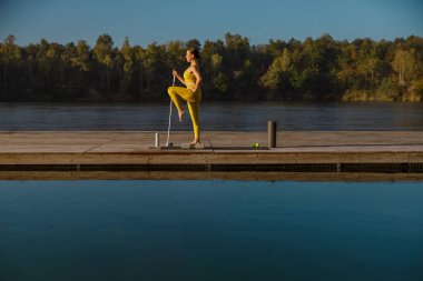 Huzurlu bir rıhtımda yoga yapmak, güzel bir doğal ortamda denge ve sükunet sergilemek.