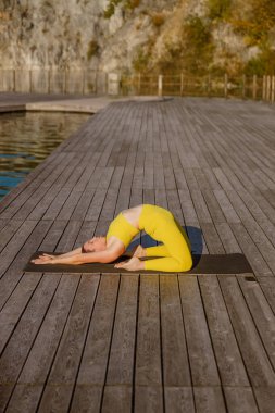 Bir insan, dingin göl kenarı ortamında yoga yapmakla meşgul. Güzelce sergilenen sükunet ve odaklanma.