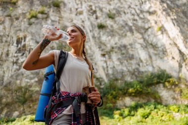 Bir kadın, güzel, sakin dağlık bir bölgede yürüyüş yaparken ferahlatıcı bir su içmekten mutlu olur.