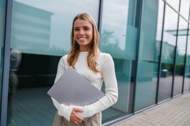 Neşeli genç bir kadın, hem profesyonelliği hem de özgüveni somutlaştıran önemli belgelerle güvenle ayakta duruyor.