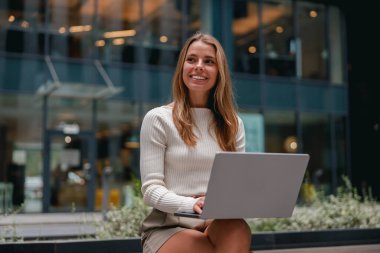 Neşeli bir kadın, modern bir ofiste dizüstü bilgisayarıyla çalışıyor. Kendini adamışlığını ve yaratıcılığını gösteriyor.