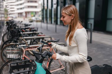 Çok sayıda parketmiş bisikleti olan canlı, modern bir şehirde genç bir kadın bisiklete binmek için kilidini açıyor.